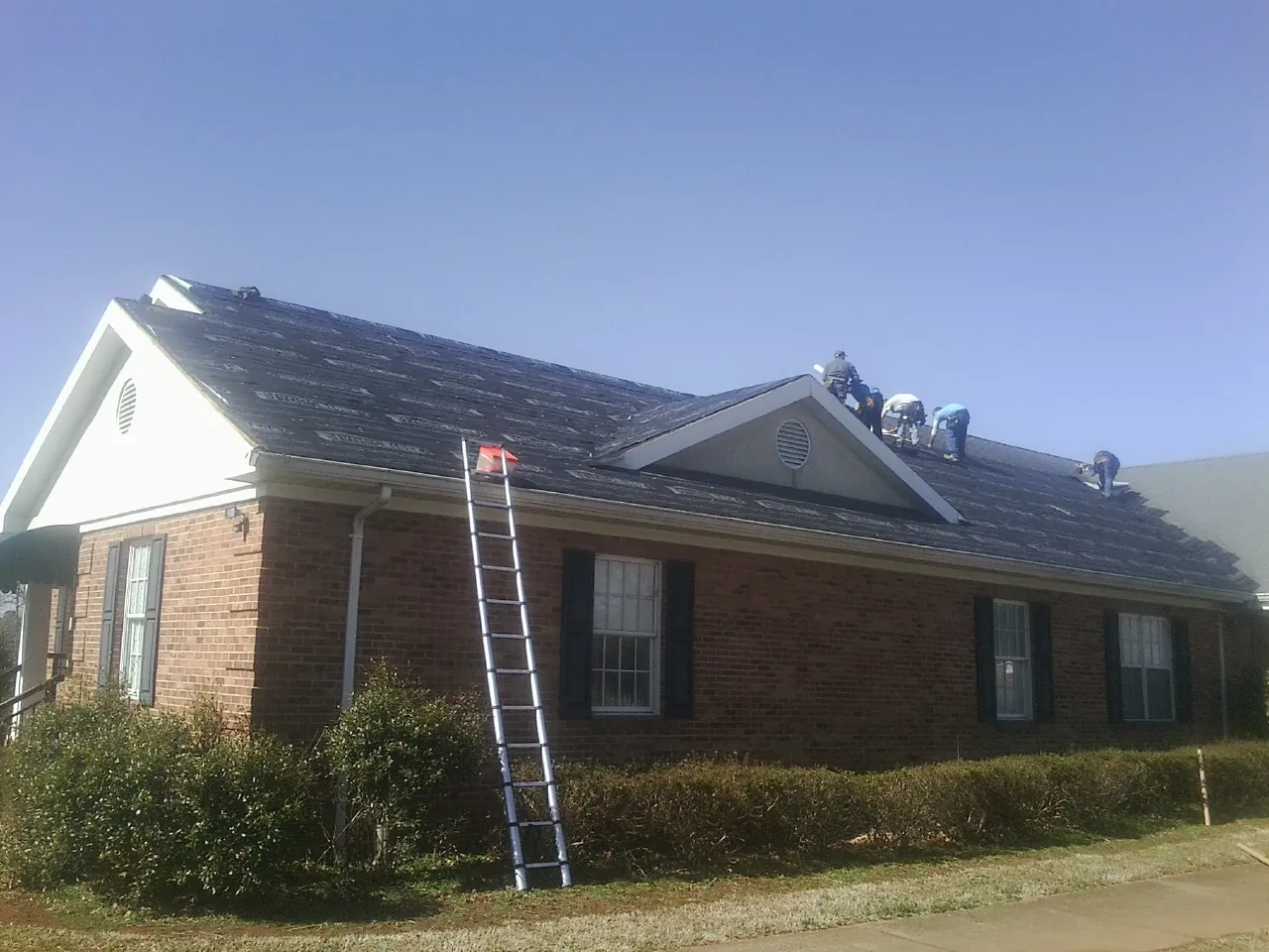 Crew tearing shingles off a brick ranch roof with a ladder set — Emergency Roof Repair work by our crew in Mc Kee