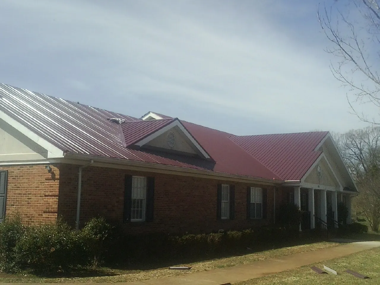 Red metal roof with gabled entries on a long brick building, from a Hail Damage Roof Repair job in Mc Kee