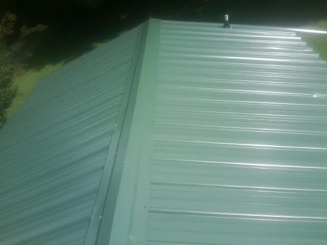 New green metal panels meeting at the ridge of a roof — Flat Roof Repair work by our crew in Mc Kee
