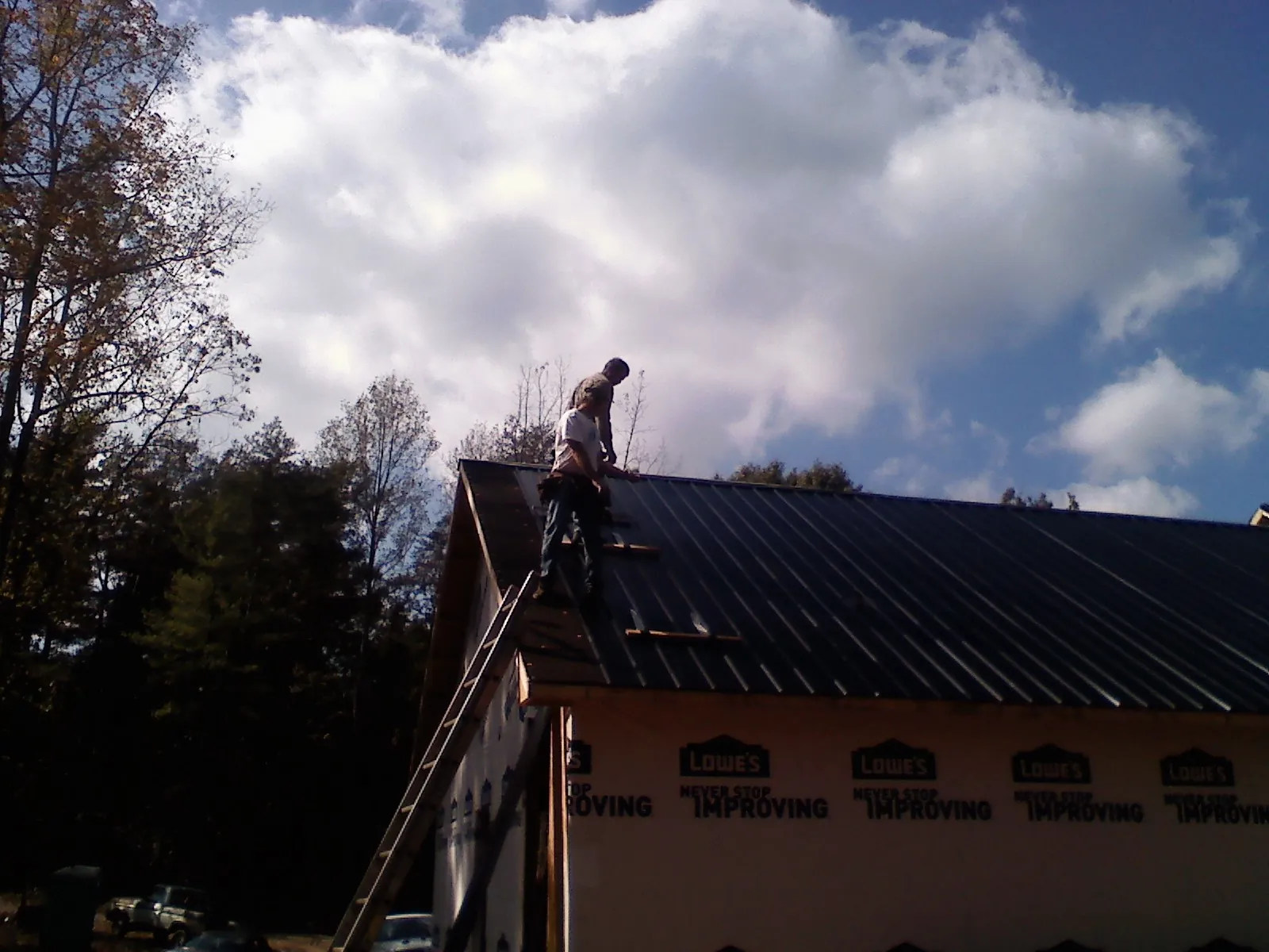 Roofer fastening dark metal panels high against a cloudy sky, from a Roof Inspection job in Mc Kee
