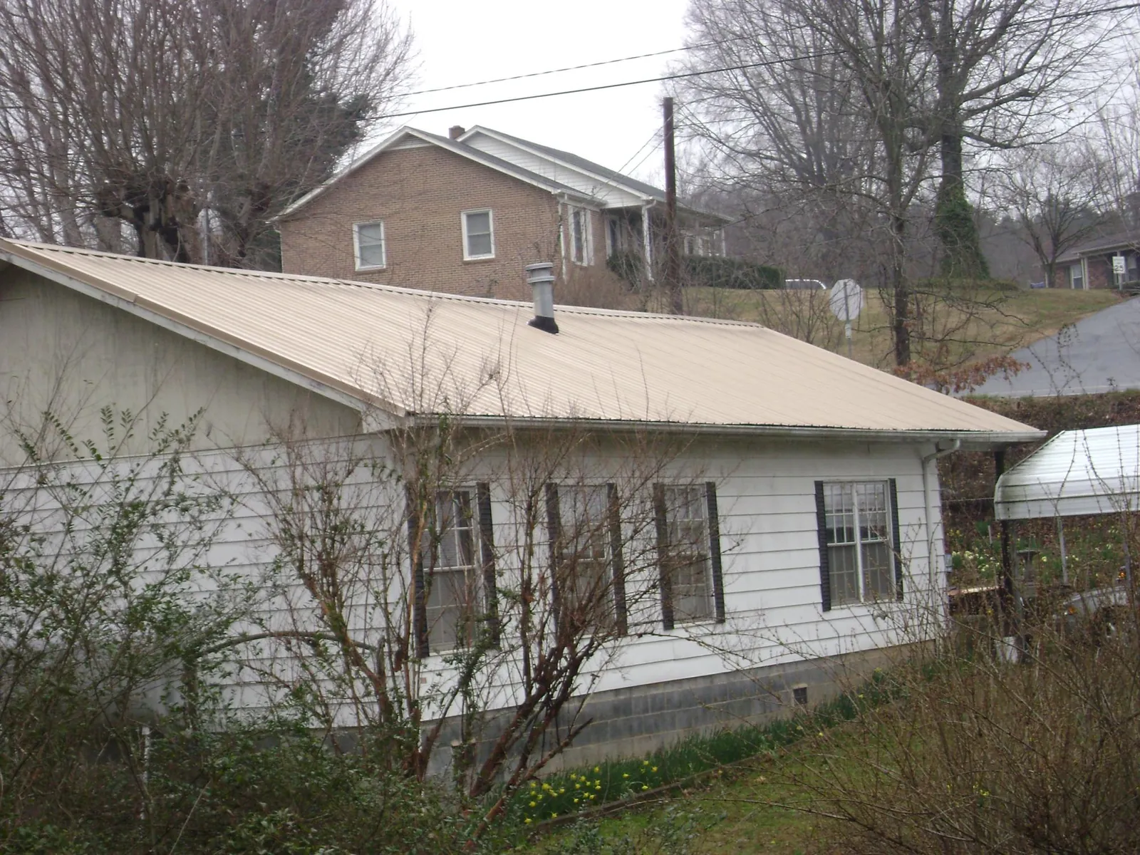Tan metal roof on a white sided house set into a hillside — Commercial Roofing by Roofing Brothers in Mc Kee
