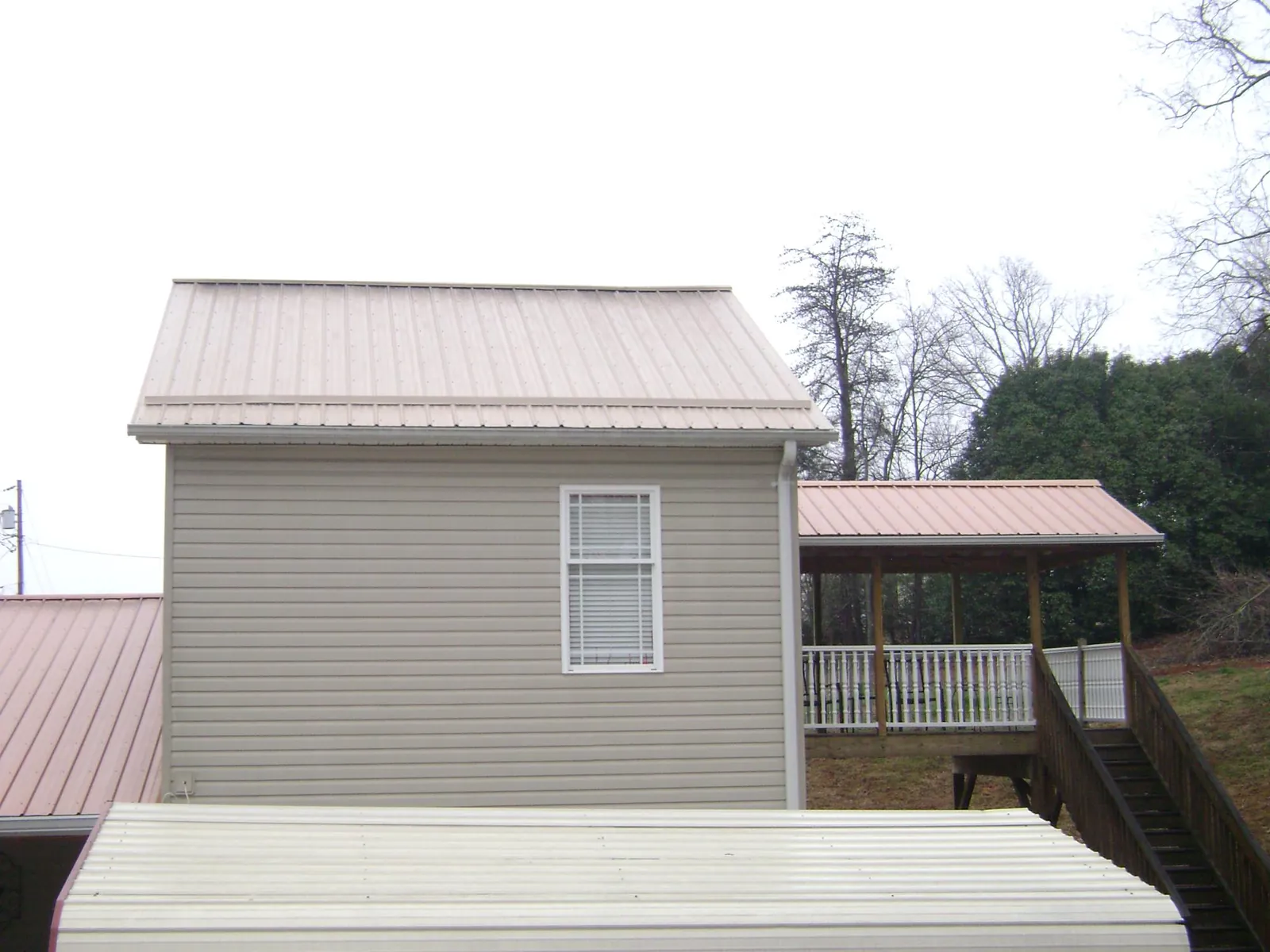 Tan metal roofs on a two story addition and attached porch, from a Roof Replacement job in Mc Kee
